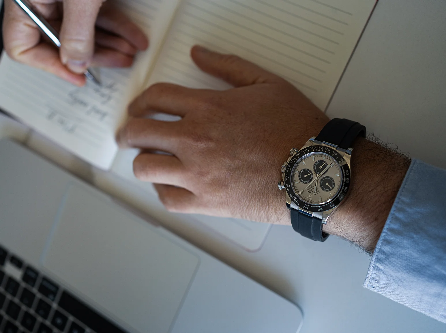 A hand writing notes in a ledger beside a chronograph on a leather strap